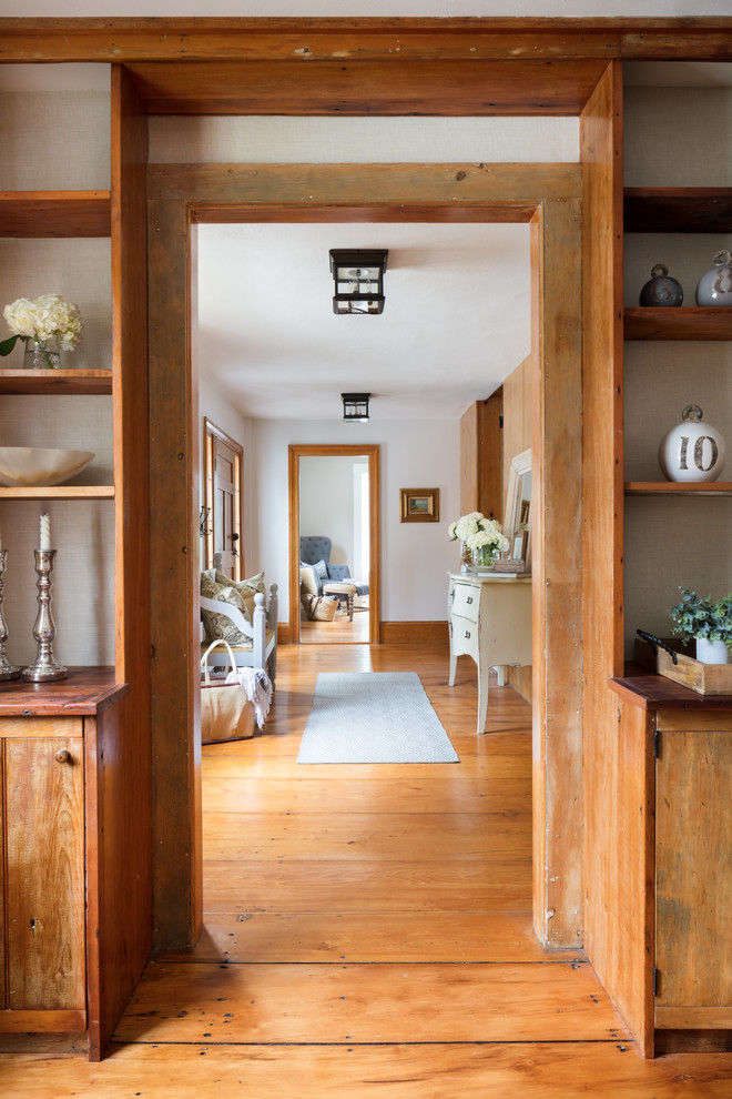 Modelo de hall campestre pequeño con paredes blancas, suelo de madera en tonos medios, puerta simple, puerta de madera en tonos medios y suelo marrón