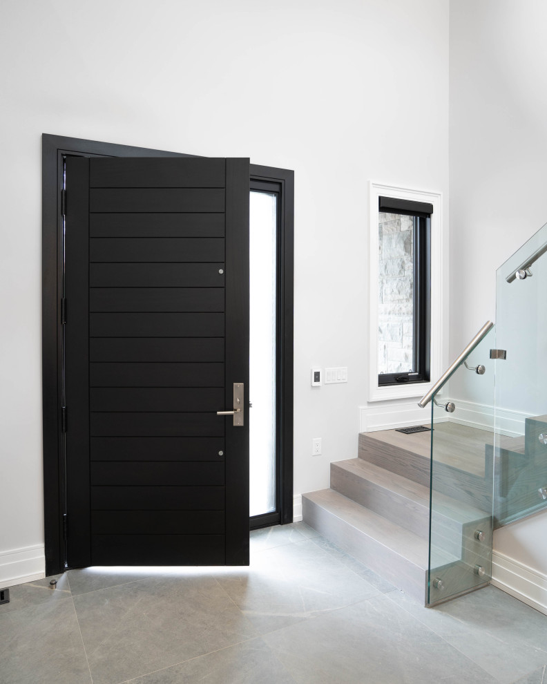 Пример оригинального дизайна: большое фойе в стиле модернизм с черной входной дверью, белыми стенами, одностворчатой входной дверью, серым полом, полом из керамогранита и многоуровневым потолком