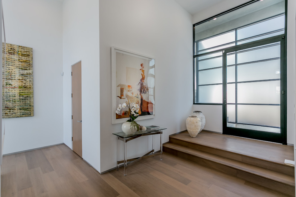 Ispirazione per un ingresso contemporaneo con pareti bianche, pavimento in legno massello medio, una porta a pivot e una porta in vetro