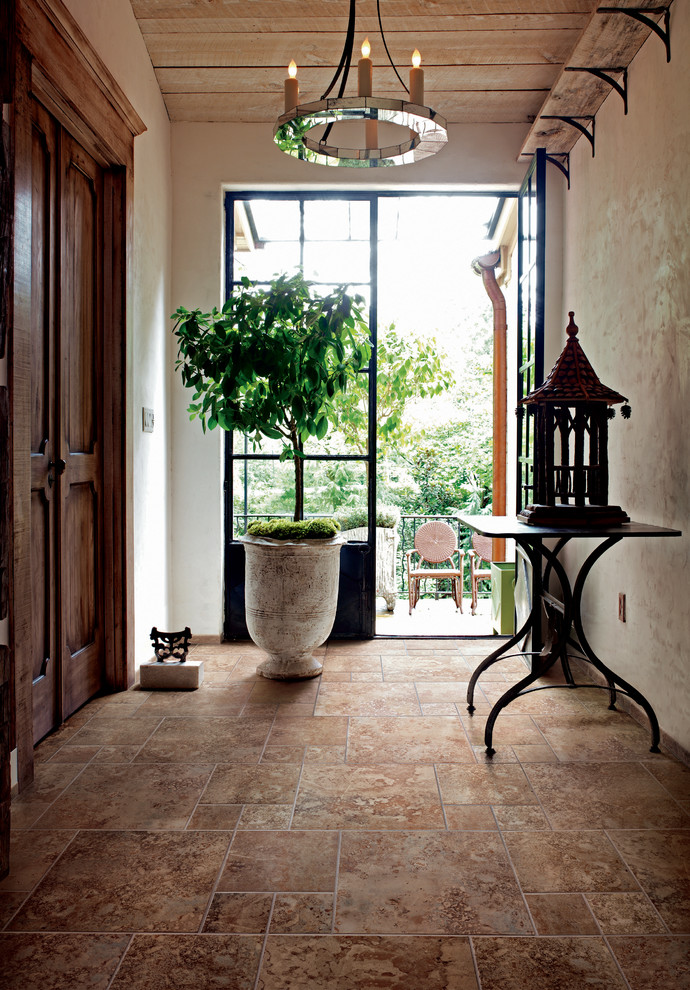 На фото: узкая прихожая среднего размера в средиземноморском стиле с бежевыми стенами, полом из керамогранита, одностворчатой входной дверью, белой входной дверью и коричневым полом с