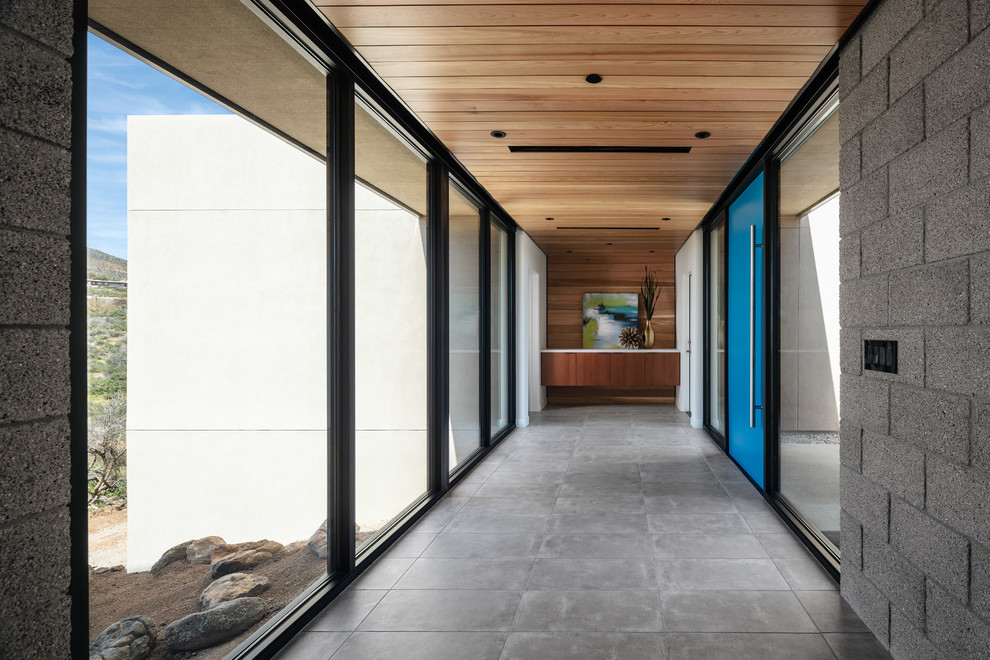 Inspiration pour une porte d'entrée design avec un mur gris, un sol en carrelage de porcelaine, une porte pivot, une porte bleue et un sol gris.