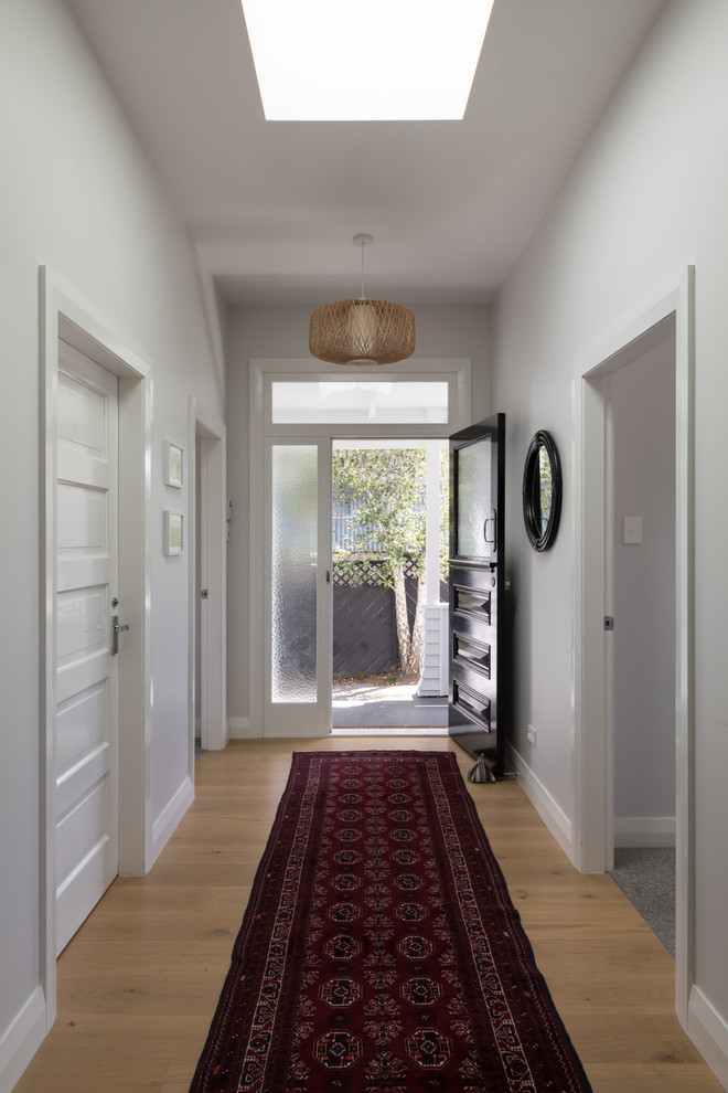 Esempio di un corridoio design di medie dimensioni con pareti bianche, pavimento in legno massello medio, una porta singola, una porta nera e pavimento marrone