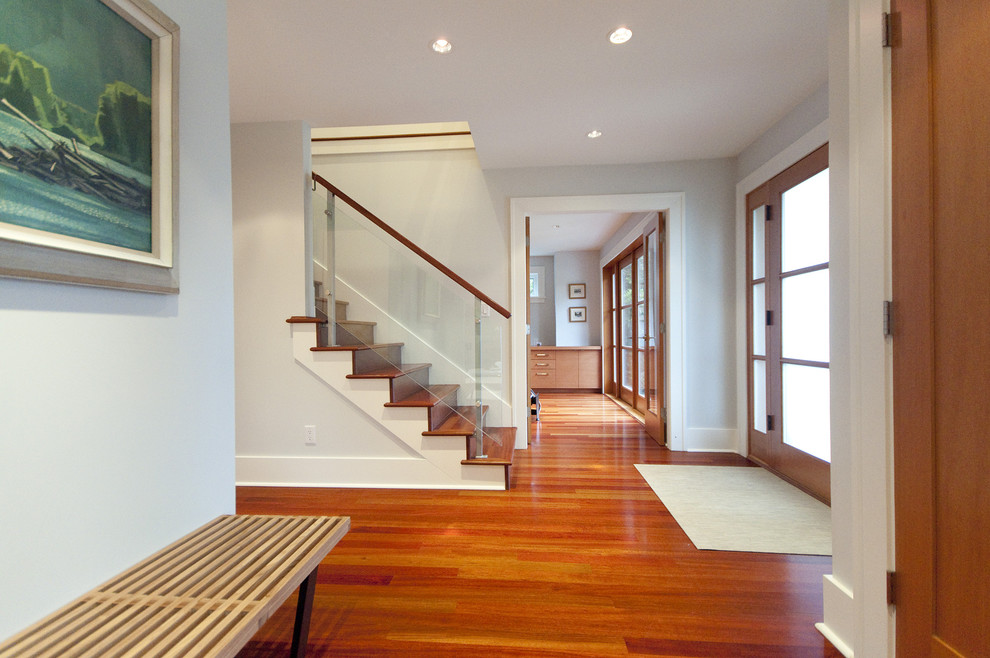 Modernes Foyer mit braunem Holzboden, Einzeltür, Haustür aus Glas und orangem Boden in Vancouver