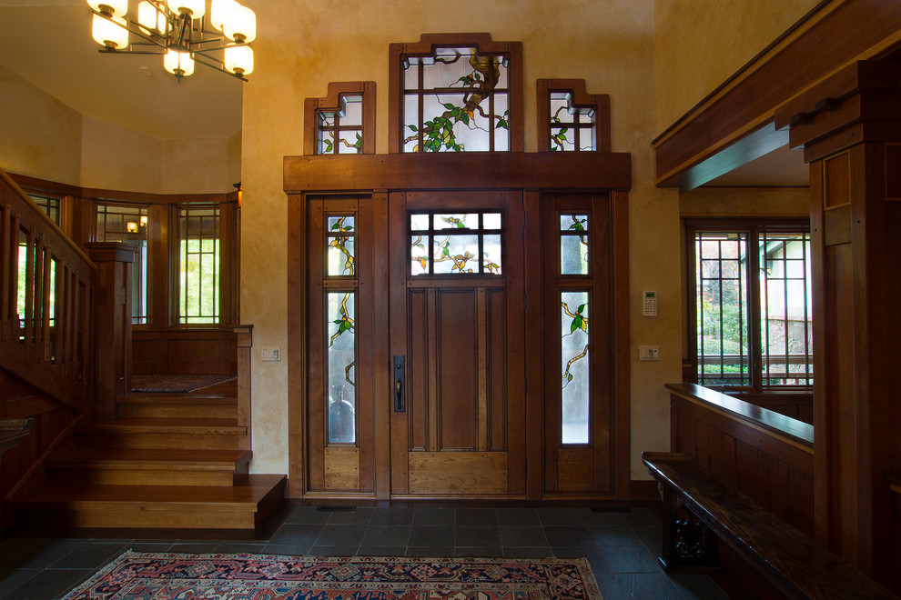 Cette photo montre un grand hall d'entrée craftsman avec un mur beige, un sol en ardoise, une porte simple et une porte en bois brun.