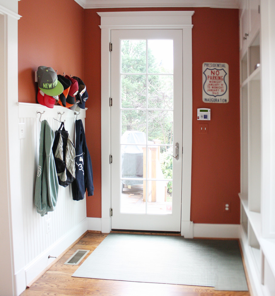 Aménagement d'une entrée classique de taille moyenne avec un vestiaire, un mur rouge, un sol en bois brun, une porte simple et une porte blanche.