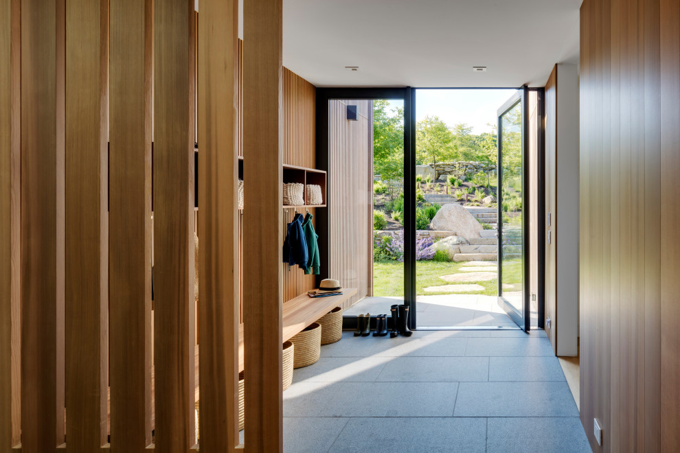 Cette photo montre une grande entrée tendance en bois avec un mur marron, une porte pivot, une porte en verre, un sol gris et un vestiaire.