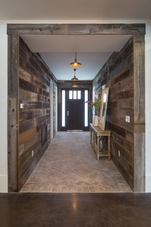 Industriell inredning av en stor ingång och ytterdörr, med bruna väggar, tegelgolv, en enkeldörr och mörk trädörr