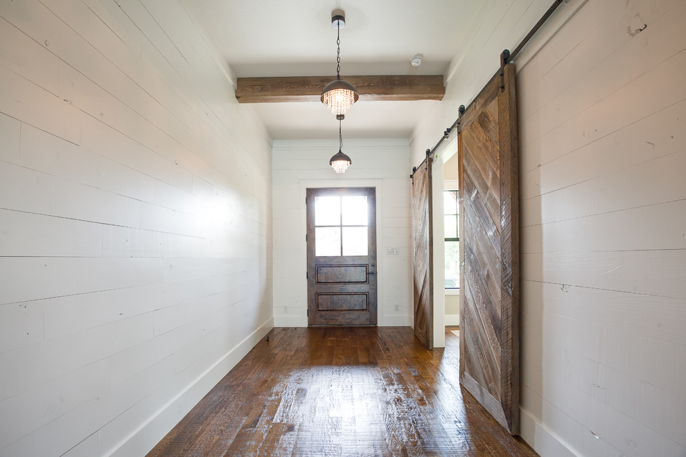 Réalisation d'une grande porte d'entrée champêtre avec un mur blanc, un sol en bois brun, une porte simple, une porte en bois foncé et un sol marron.