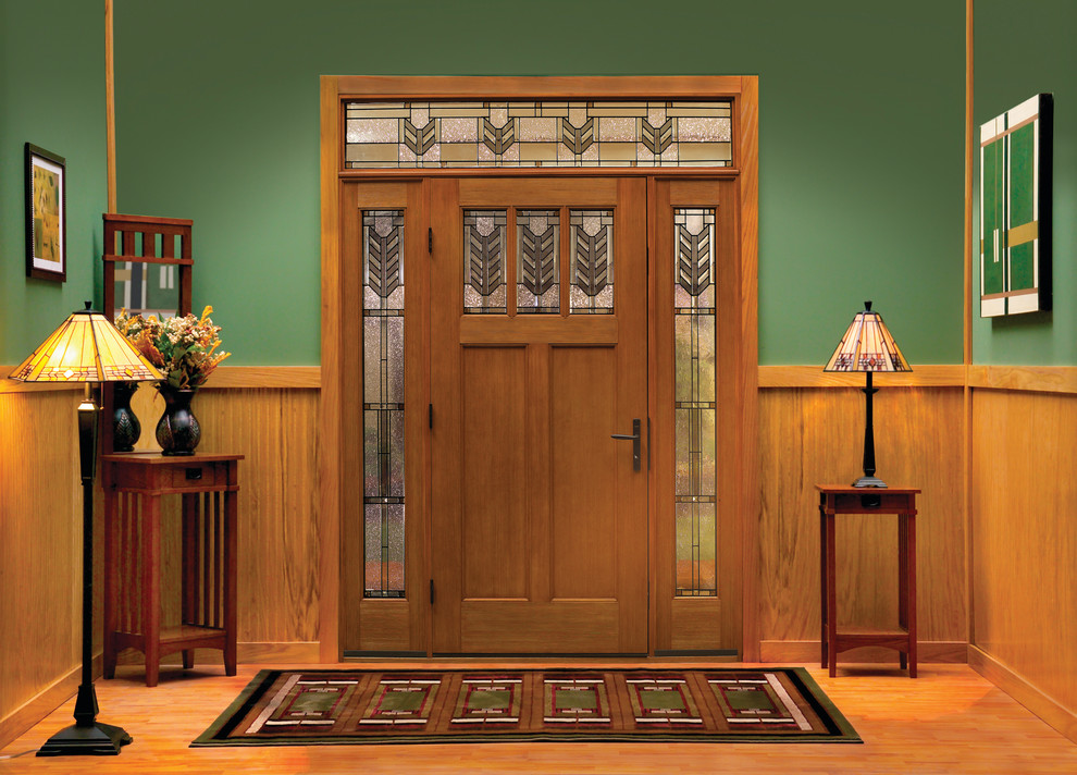 Cette image montre une porte d'entrée craftsman avec un mur vert, une porte simple, une porte en bois brun et un sol en bois brun.
