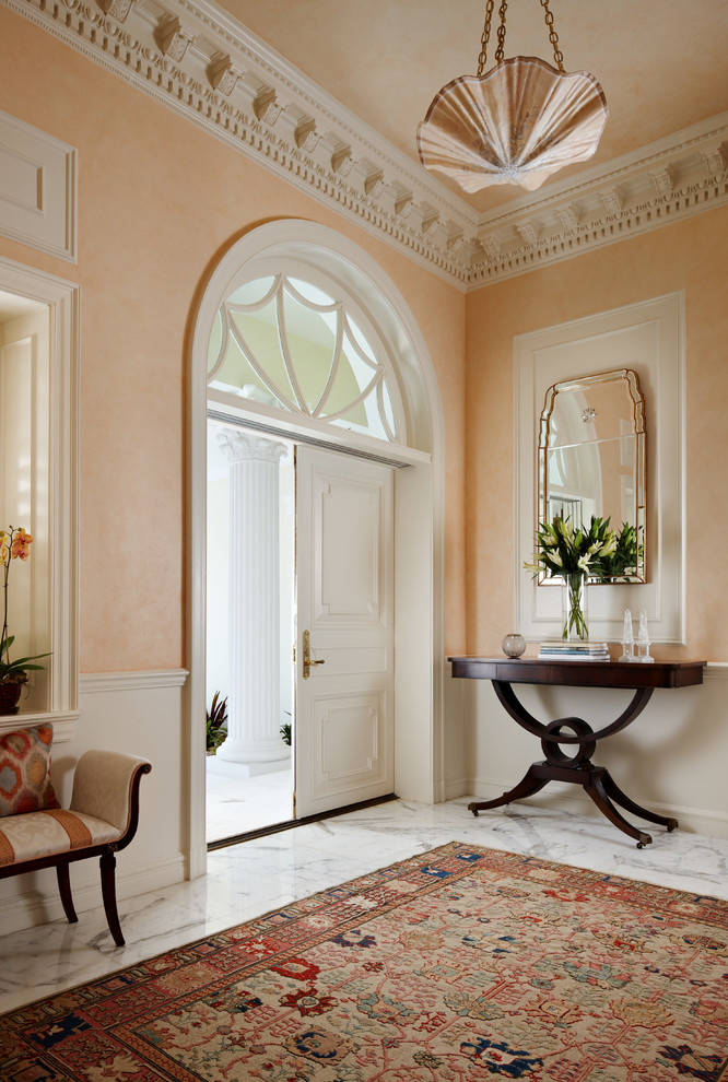 Réalisation d'un grand hall d'entrée tradition avec un mur orange, un sol en marbre, une porte double, une porte blanche et un sol gris.