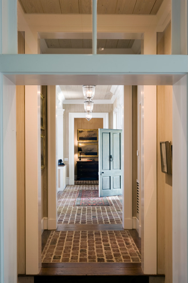 Cette photo montre une entrée chic avec un couloir, un mur beige, un sol en brique, une porte simple et une porte blanche.