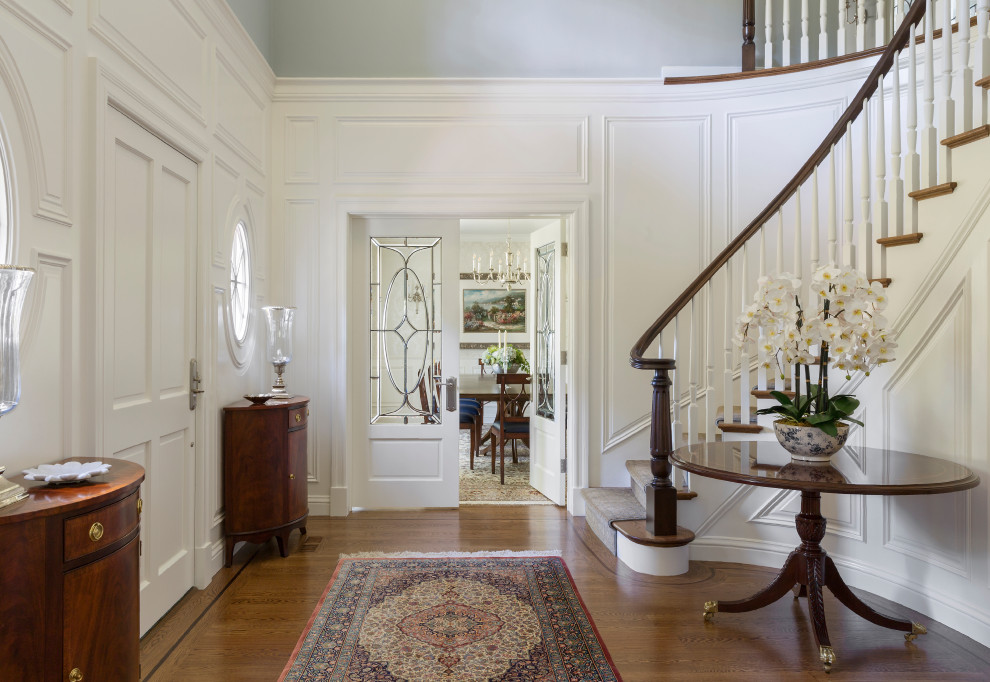 Esempio di un ingresso classico con pareti bianche, pavimento in legno massello medio, una porta singola, una porta bianca, pavimento marrone e pannellatura