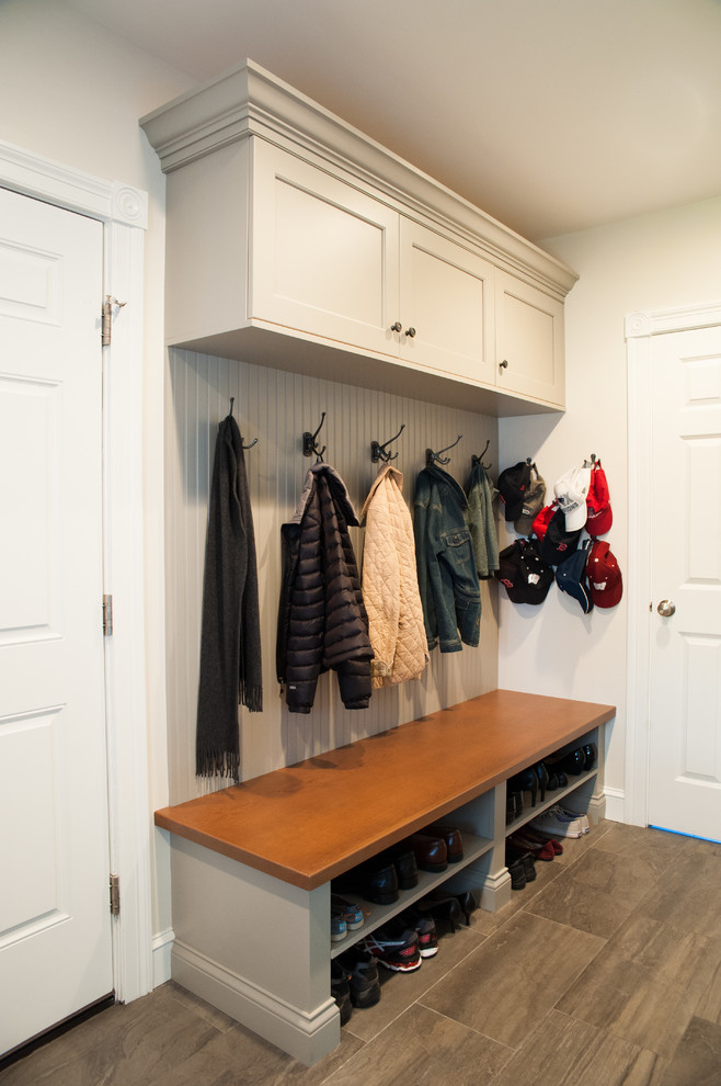 На фото: тамбур среднего размера со шкафом для обуви в стиле неоклассика (современная классика) с бежевыми стенами, полом из керамической плитки, одностворчатой входной дверью, белой входной дверью и коричневым полом с