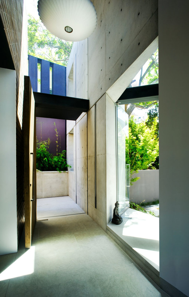 Réalisation d'une grande porte d'entrée minimaliste avec un mur blanc, sol en béton ciré, une porte pivot et une porte en bois brun.