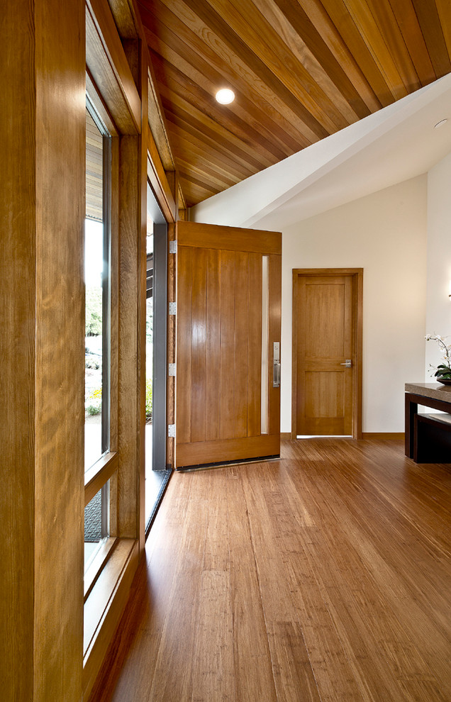 Cette photo montre un grand hall d'entrée tendance avec un mur blanc, parquet en bambou, une porte simple et une porte en bois clair.