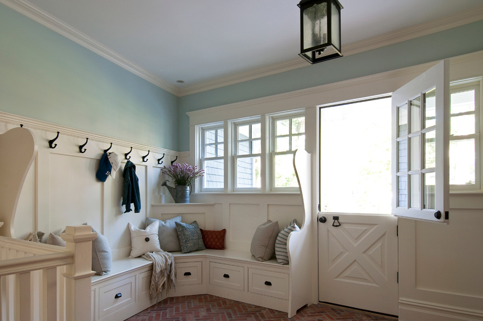 Lantlig inredning av ett mellanstort kapprum, med blå väggar, tegelgolv, en tvådelad stalldörr, en vit dörr och brunt golv