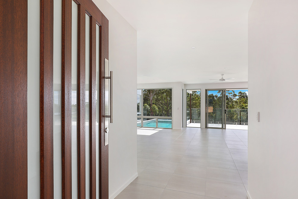 Foto di un grande ingresso minimalista con pareti bianche, pavimento con piastrelle in ceramica, una porta a pivot, una porta in legno scuro e pavimento beige