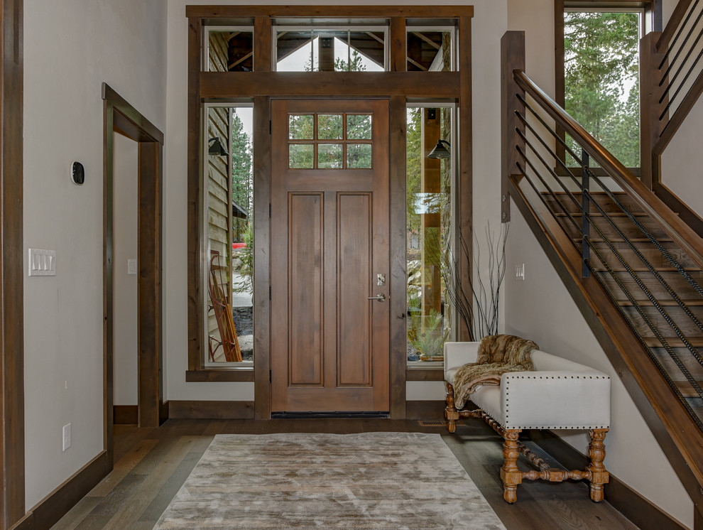 Cette image montre un hall d'entrée chalet avec un mur blanc, parquet foncé, une porte simple, une porte en bois foncé et un sol marron.