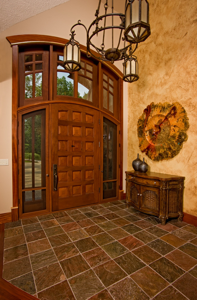 Aménagement d'un grand hall d'entrée montagne avec un sol en ardoise, une porte simple, une porte en bois brun et un mur beige.