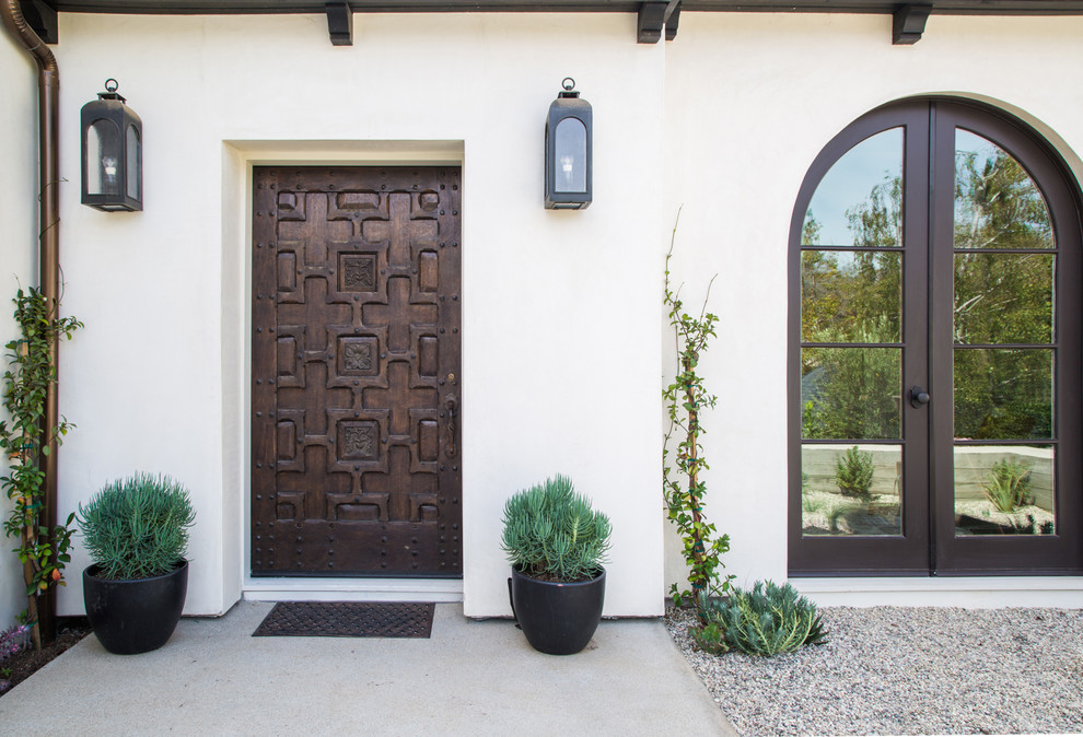 На фото: входная дверь в средиземноморском стиле с белыми стенами, бетонным полом, одностворчатой входной дверью и входной дверью из темного дерева