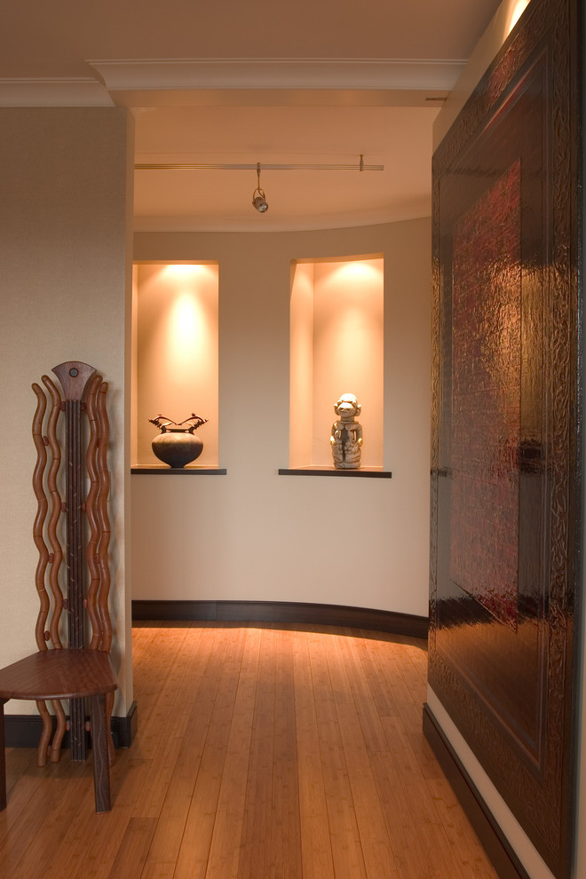 Cette image montre une entrée design avec un couloir, un mur beige, parquet en bambou et une porte pivot.