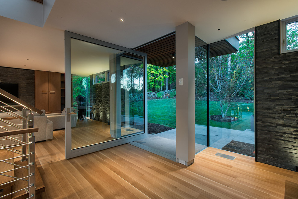 Réalisation d'un hall d'entrée design avec un sol en bois brun, une porte pivot, une porte en verre et un sol marron.