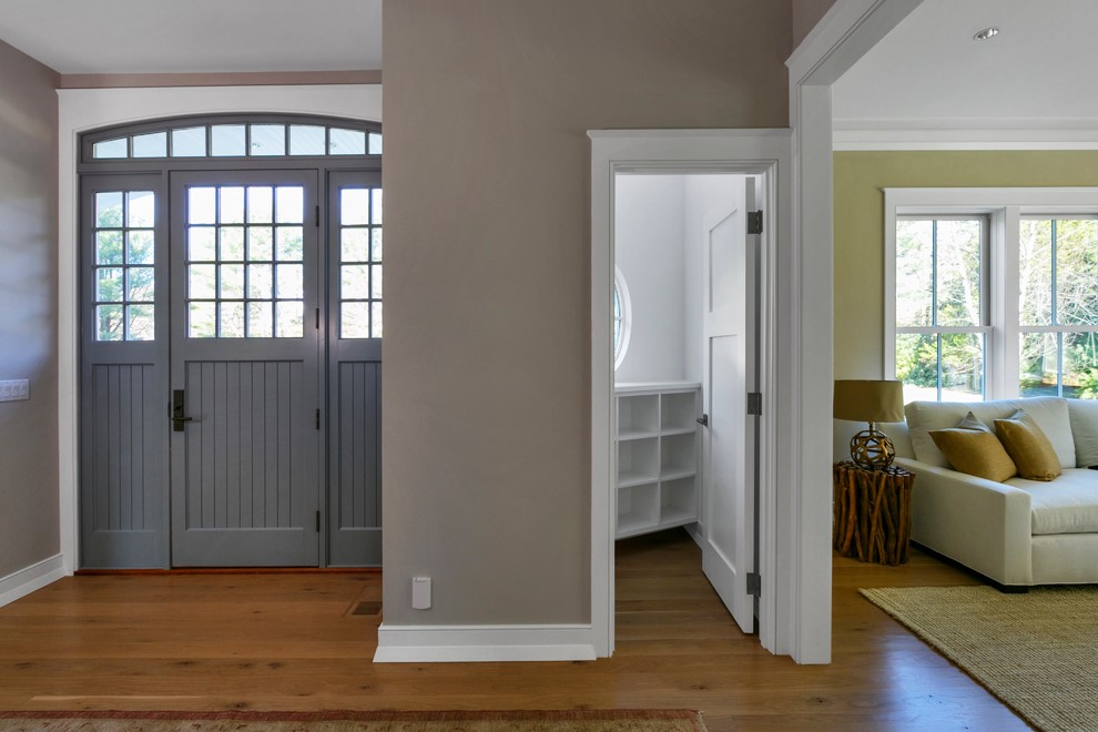 Inredning av en modern stor ingång och ytterdörr, med beige väggar, ljust trägolv, en enkeldörr och en grå dörr