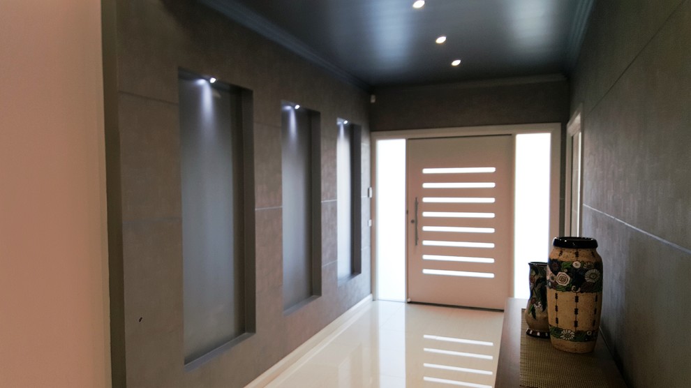 Cette photo montre un hall d'entrée tendance de taille moyenne avec mur métallisé, un sol en carrelage de porcelaine, une porte simple et une porte blanche.