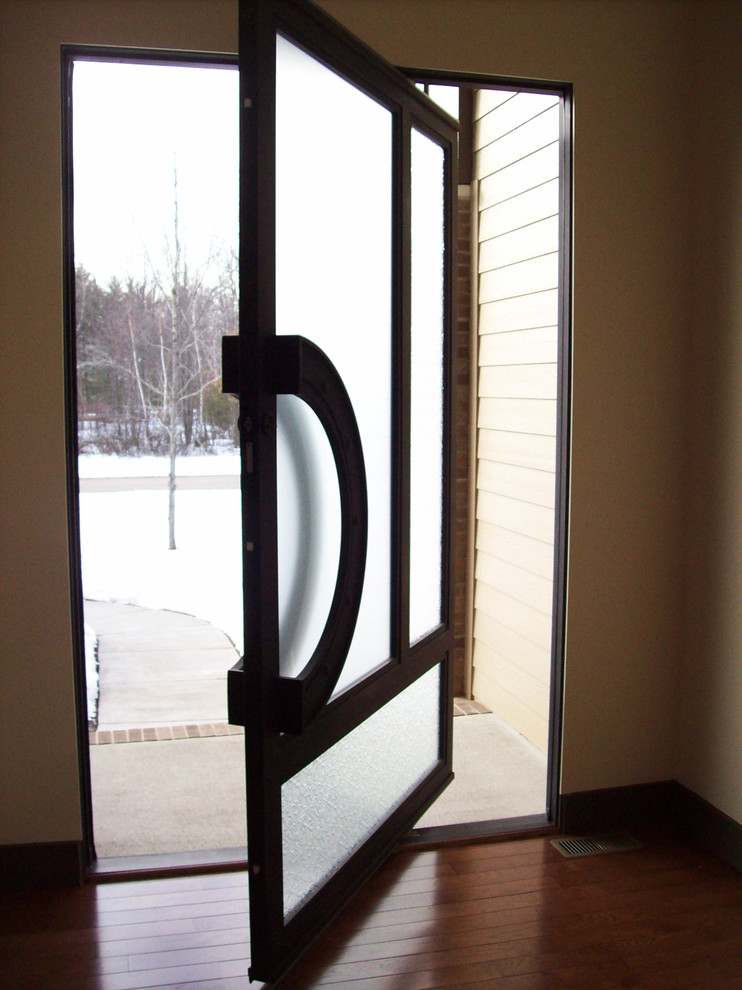 Aménagement d'une grande porte d'entrée contemporaine avec un mur beige, parquet foncé, une porte pivot et une porte en verre.