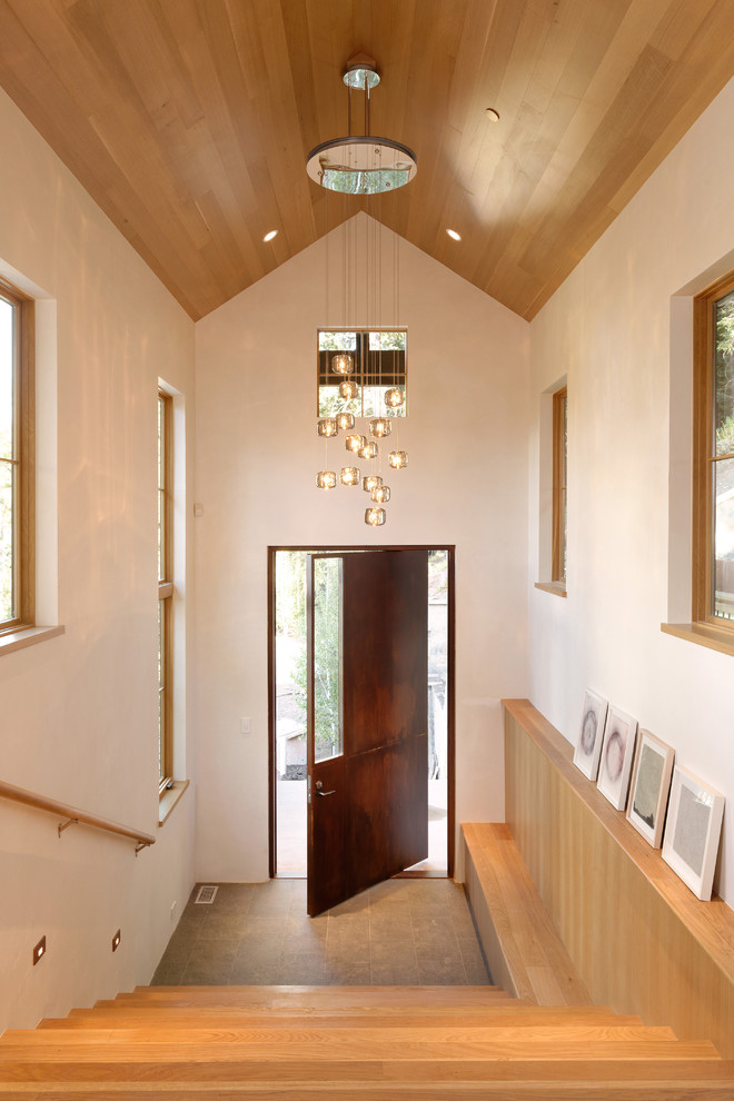 Cette image montre une entrée design avec un mur blanc, parquet clair, une porte pivot et une porte marron.