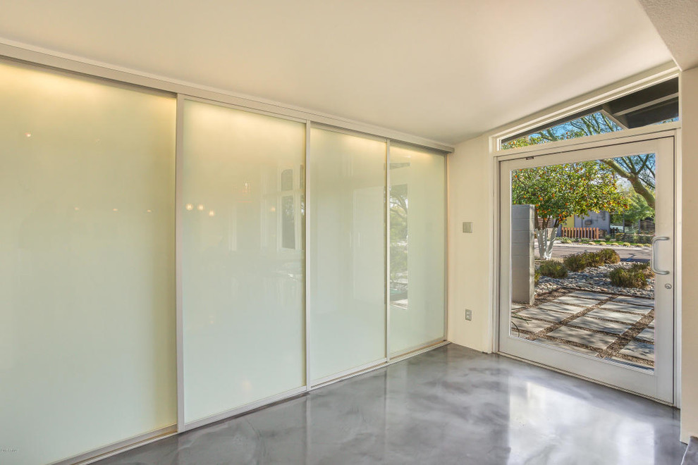 Idee per una grande porta d'ingresso minimal con pavimento in cemento, una porta singola, una porta in vetro, pareti bianche e pavimento grigio
