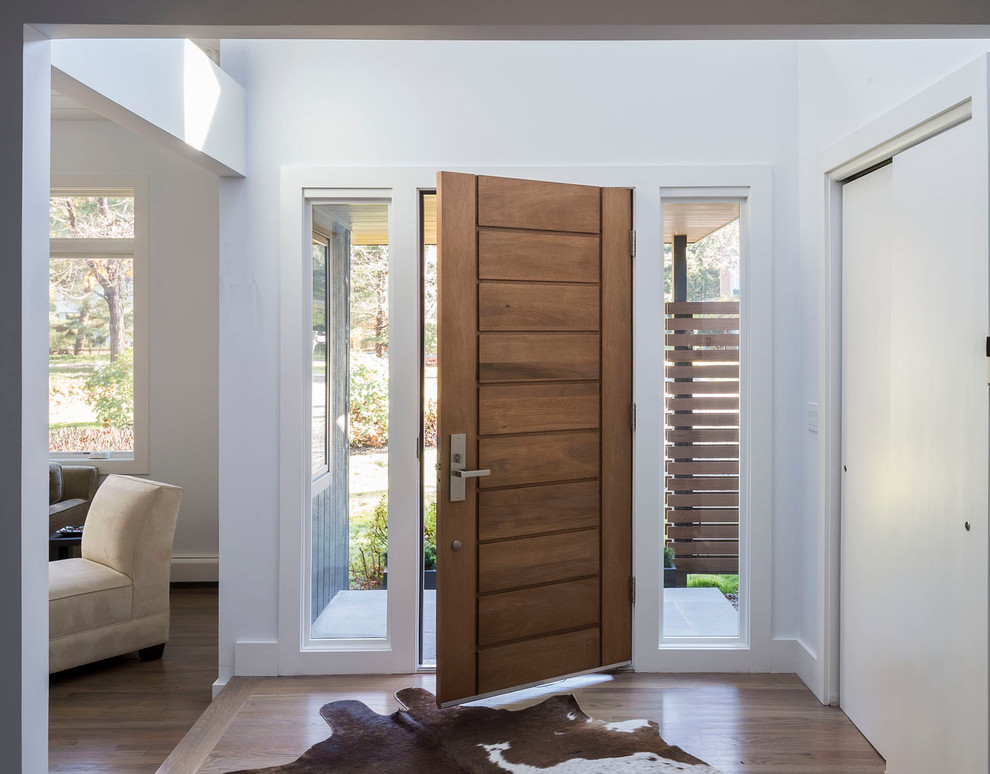 Ejemplo de distribuidor actual de tamaño medio con paredes blancas, suelo de madera clara, puerta simple y puerta de madera en tonos medios