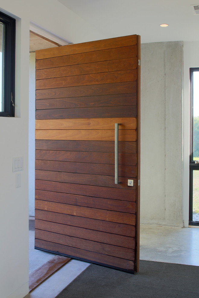 На фото: входная дверь среднего размера в современном стиле с белыми стенами, бетонным полом, поворотной входной дверью, входной дверью из темного дерева и серым полом
