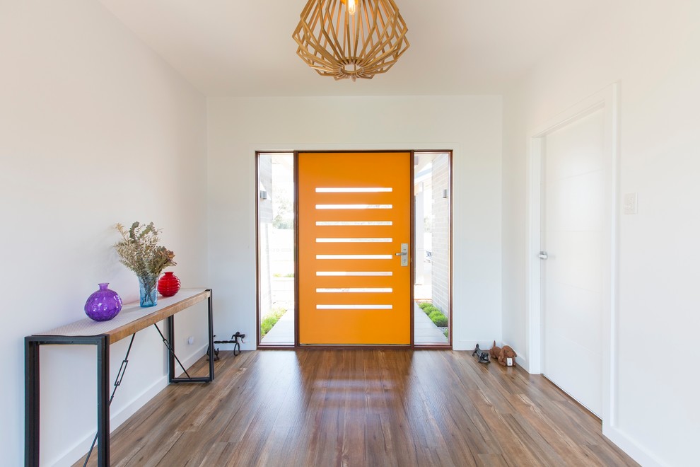 Aménagement d'un grand hall d'entrée contemporain avec un mur blanc, un sol en bois brun, une porte simple et une porte orange.