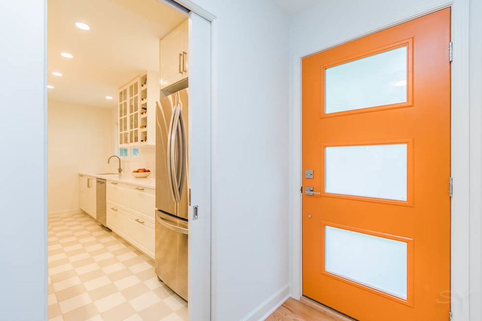 Bild på en 50 tals entré, med vita väggar, ljust trägolv och en orange dörr