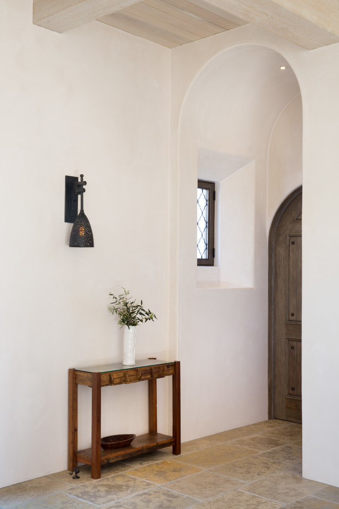Immagine di una piccola porta d'ingresso mediterranea con pareti bianche, pavimento in pietra calcarea, pavimento beige, una porta singola e una porta in legno bruno