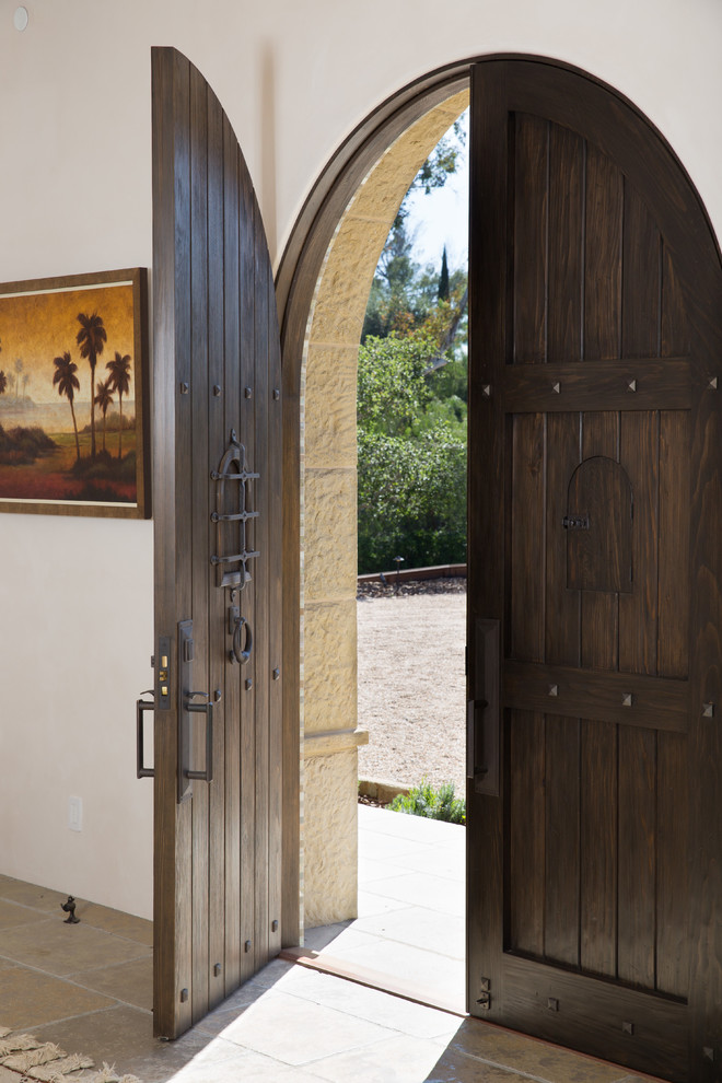 Стильный дизайн: большое фойе в средиземноморском стиле с белыми стенами, полом из известняка, бежевым полом, двустворчатой входной дверью и входной дверью из темного дерева - последний тренд