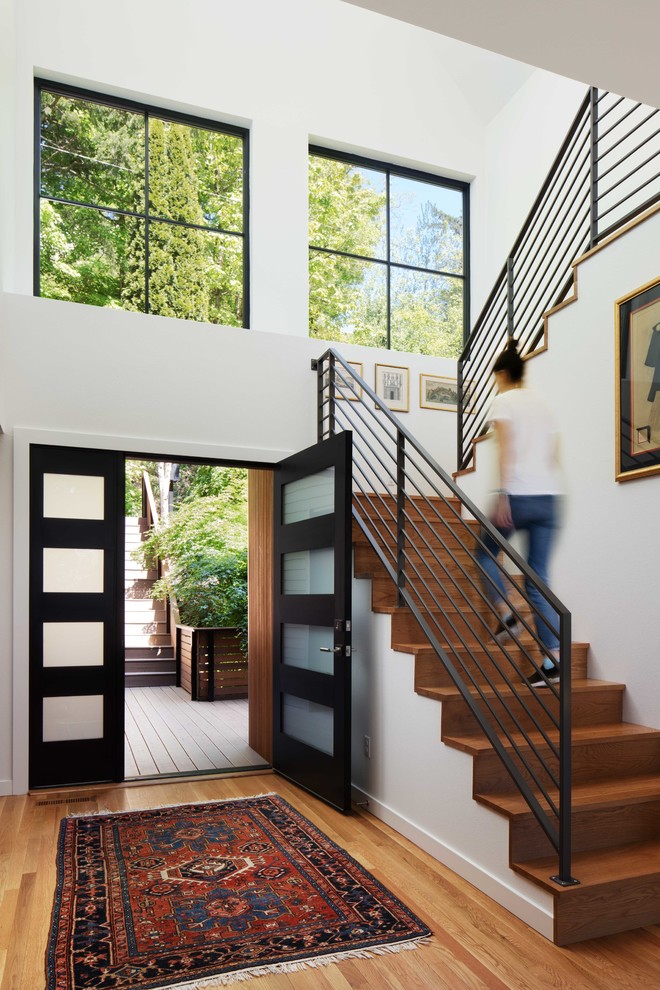 Réalisation d'une porte d'entrée design de taille moyenne avec un mur blanc, un sol en bois brun, une porte double et une porte noire.