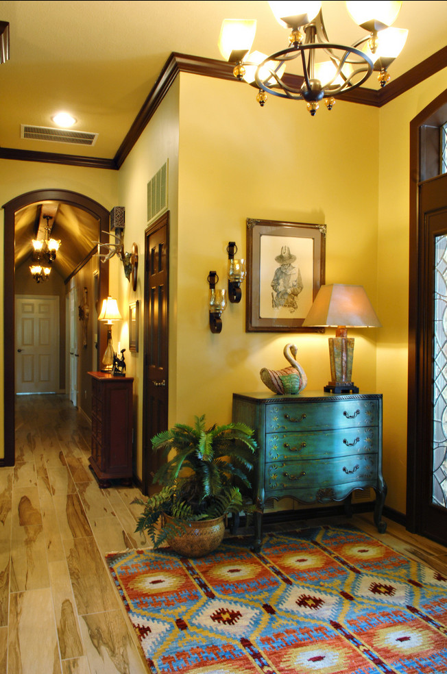 ダラスにある広いサンタフェスタイルのおしゃれな玄関ロビー (黄色い壁、淡色無垢フローリング、濃色木目調のドア) の写真