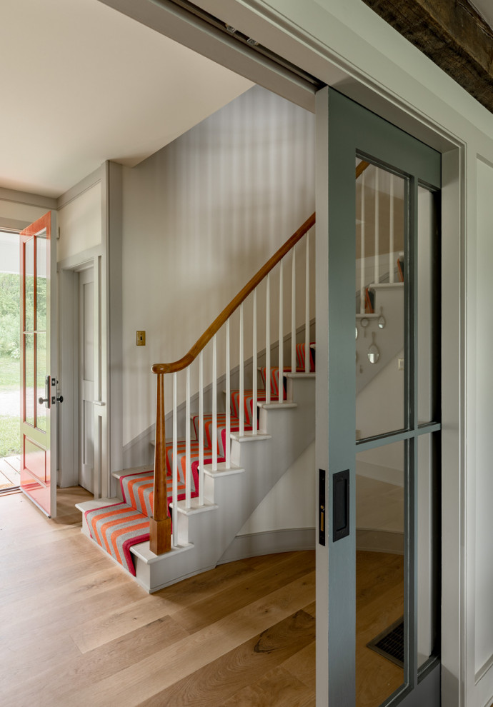Imagen de entrada campestre con paredes blancas, suelo de madera en tonos medios y puerta roja