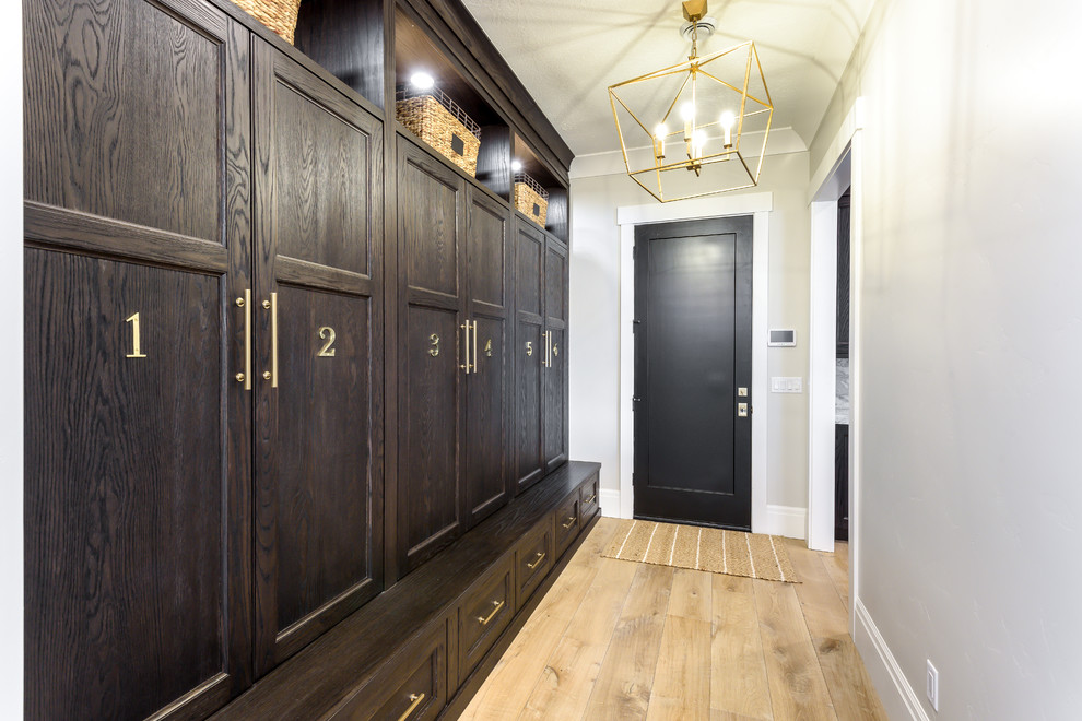 Foto på ett stort vintage kapprum, med grå väggar, ljust trägolv, en enkeldörr, en svart dörr och brunt golv