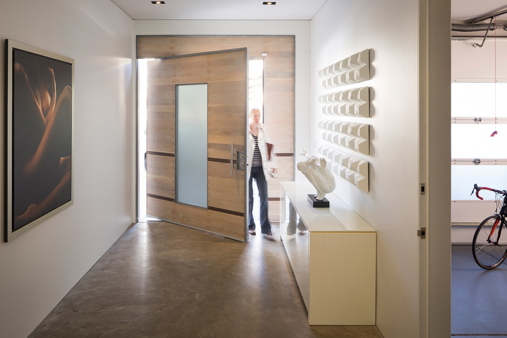 Ejemplo de distribuidor moderno grande con paredes blancas, suelo de cemento, puerta pivotante y puerta de madera clara
