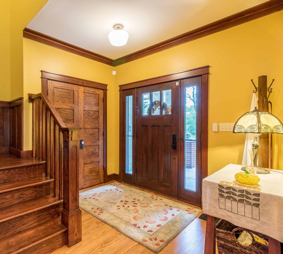 Mittelgroßes Uriges Foyer mit gelber Wandfarbe, hellem Holzboden, Einzeltür, hellbrauner Holzhaustür, braunem Boden, Treppe, Tapetendecke und Tapetenwänden in Chicago