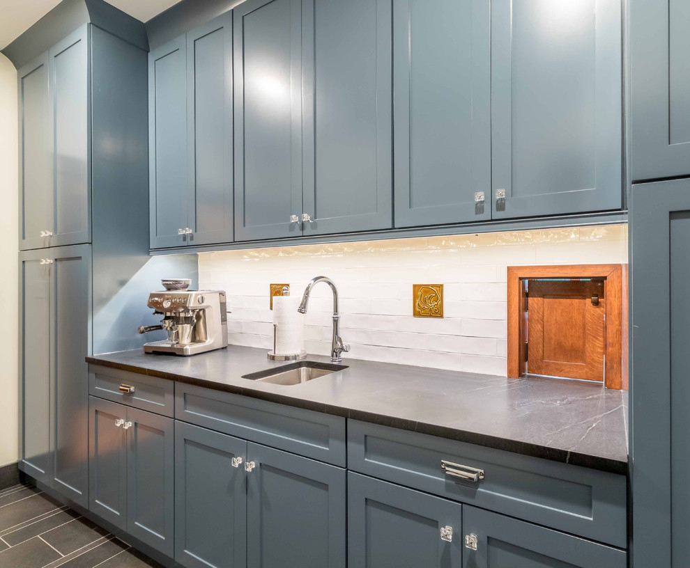 Medium sized traditional single-wall wet bar in Chicago with beaded cabinets, blue cabinets, granite worktops, black worktops, a submerged sink, white splashback, cement tile splashback, ceramic flooring, brown floors and feature lighting.