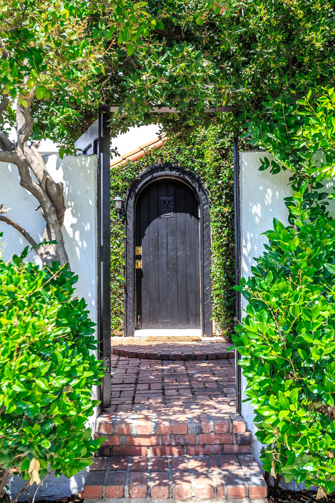 На фото: входная дверь в средиземноморском стиле с белыми стенами, кирпичным полом, одностворчатой входной дверью, черной входной дверью и красным полом