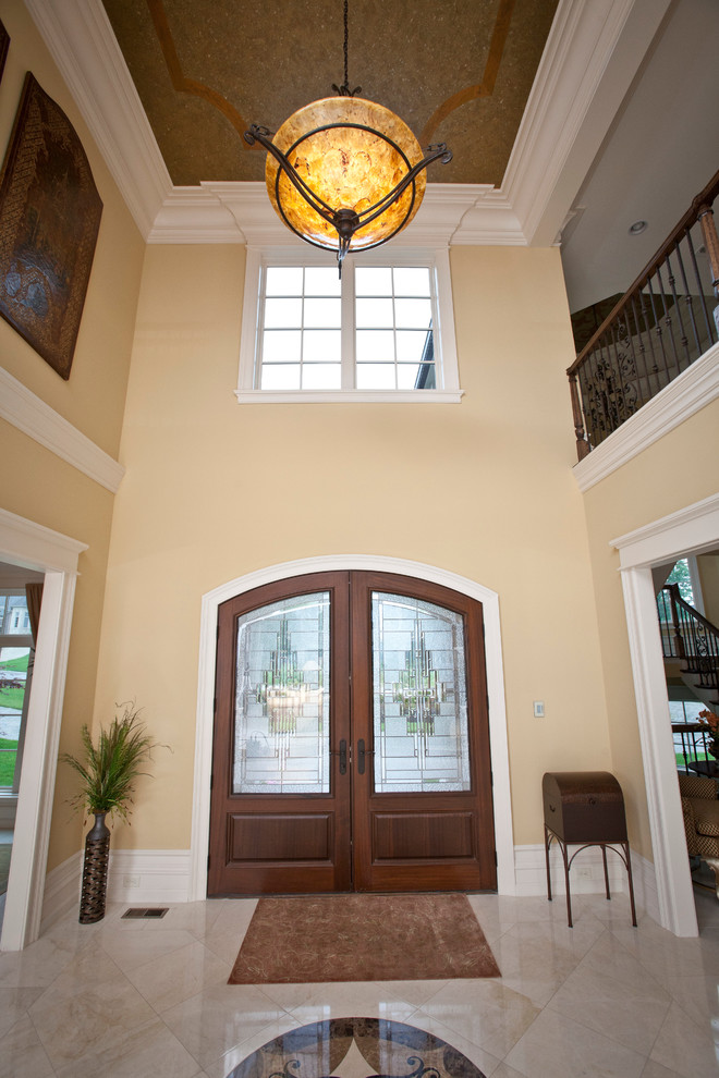 Пример оригинального дизайна: огромное фойе в классическом стиле с желтыми стенами, мраморным полом, двустворчатой входной дверью и входной дверью из темного дерева