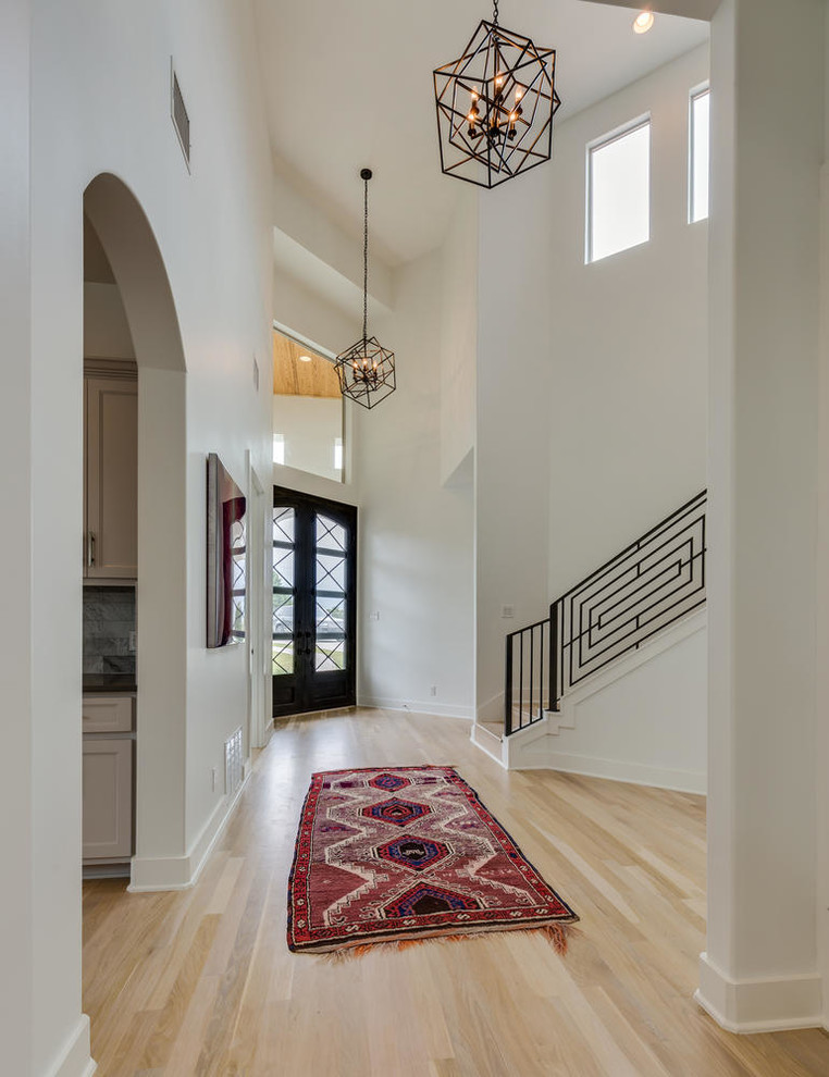 Cette photo montre une grande entrée tendance avec un couloir, un mur blanc, parquet clair, une porte double, une porte en verre et un sol marron.