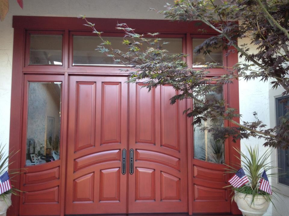 Cette image montre une très grande porte d'entrée traditionnelle avec un mur blanc, une porte double et une porte rouge.