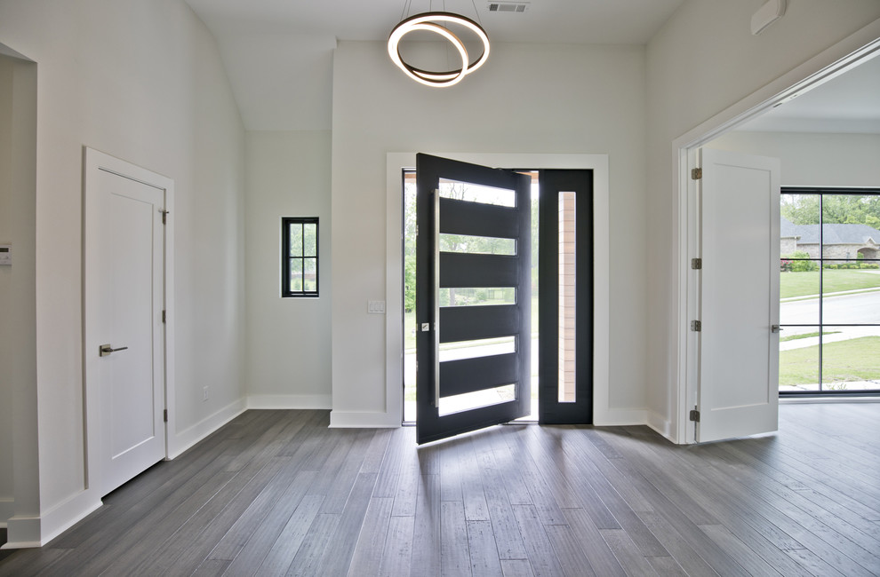 Cette photo montre une grande porte d'entrée tendance avec un mur blanc, un sol en bois brun, une porte simple, une porte noire et un sol gris.