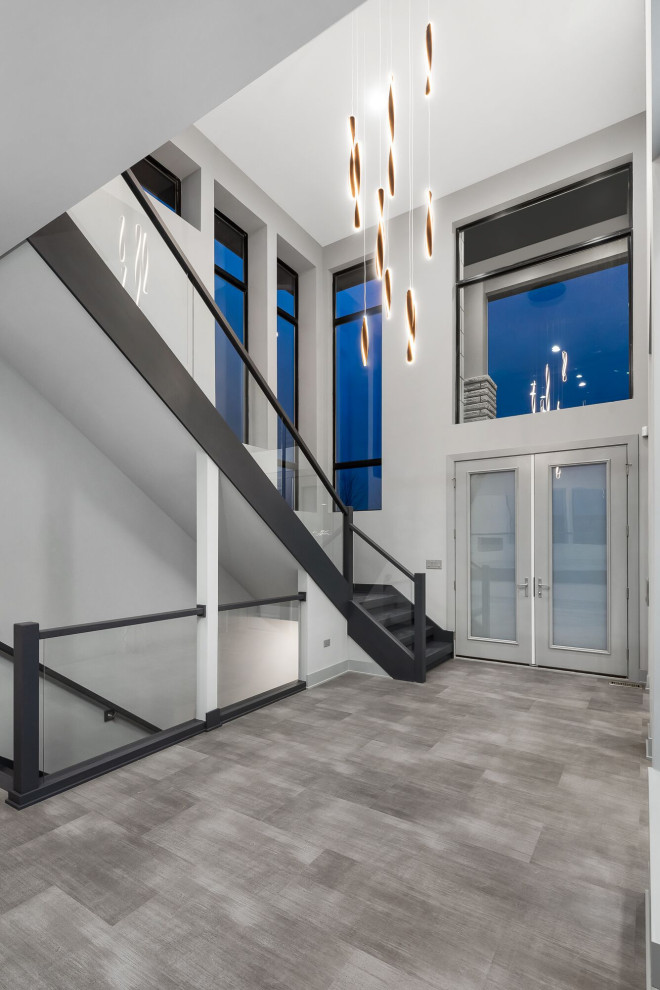 Cette image montre un grand hall d'entrée minimaliste avec un mur gris, une porte double, une porte en verre, un sol gris et un plafond voûté.